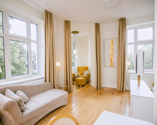 Blick in das Komfortzimmer mit Großen Fenstern, Sofa und Sessel im Hintergrund.